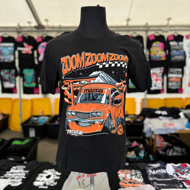 Black t-shirt with orange car graphic and 'Zoom Zoom Zoom' text on a mannequin, with a market background.